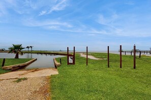 A grassy area with a water body, a wooden dock, and a signpost. - Rockport Racquet & Yacht Club - Coastline Condo (Rockport)