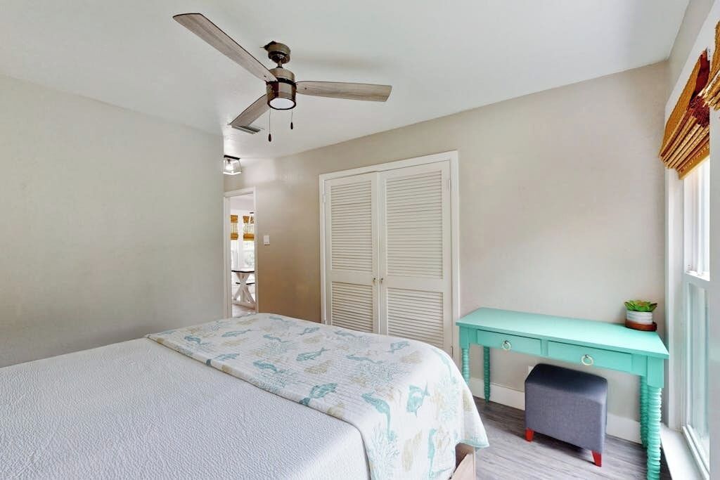 A bedroom with a bed, a ceiling fan, a wardrobe, a desk, and a window.