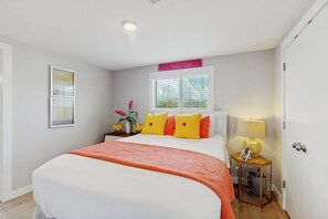 Ein Hotelzimmer mit Bett, Fenster, Nachttisch mit Lampe und einem an der Wand hängenden Kunstwerk.