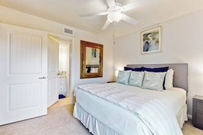 A bedroom with a bed, a ceiling fan, a door, a mirror, and a painting on the wall. - Rockport Waterfront Getaway #608 (Rockport)
