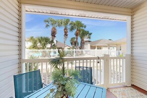 A covered outdoor area with a table and chairs, a railing, and a view of palm trees and houses in the background. - Palm Bay 407 & 408 - Two Units, Pool, Sleeps 12 (Corpus Christi)