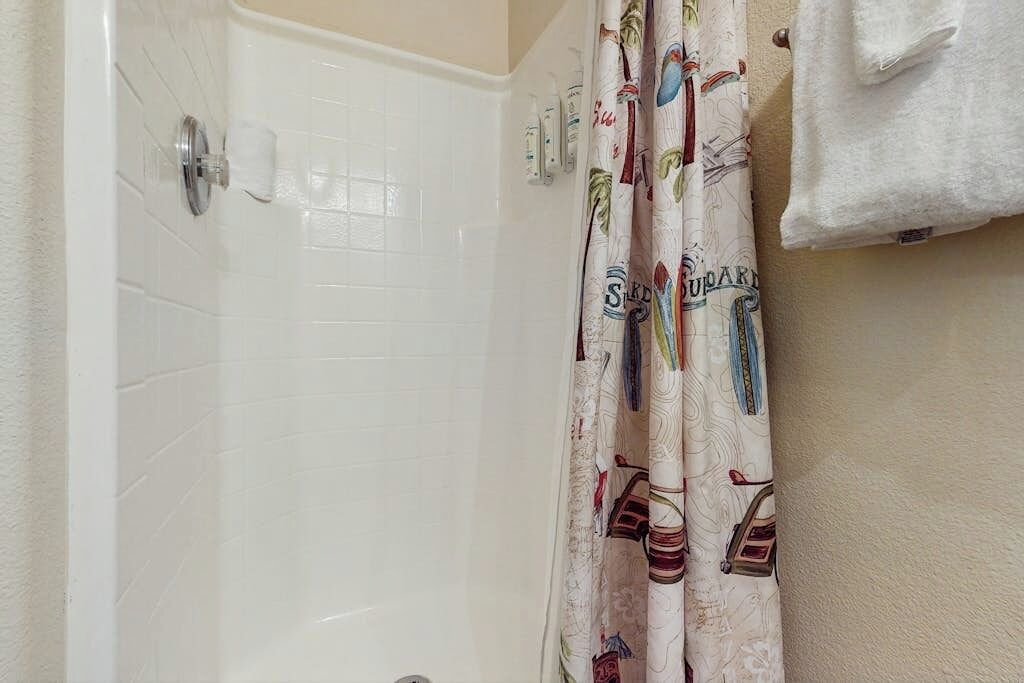 Un baño con una bañera blanca, una cortina de ducha estampada y una toalla colgada en la pared.