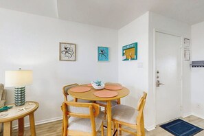 A dining area with a round table, four chairs, and a small side table with a lamp. - Beach Club 352 - Pool, Hot Tub, Gym & Balcony (Corpus Christi)