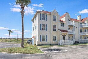 A multi-story building with a central entrance, balconies, and a parking lot. - Beach Club 352 - Pool, Hot Tub, Gym & Balcony (Corpus Christi)