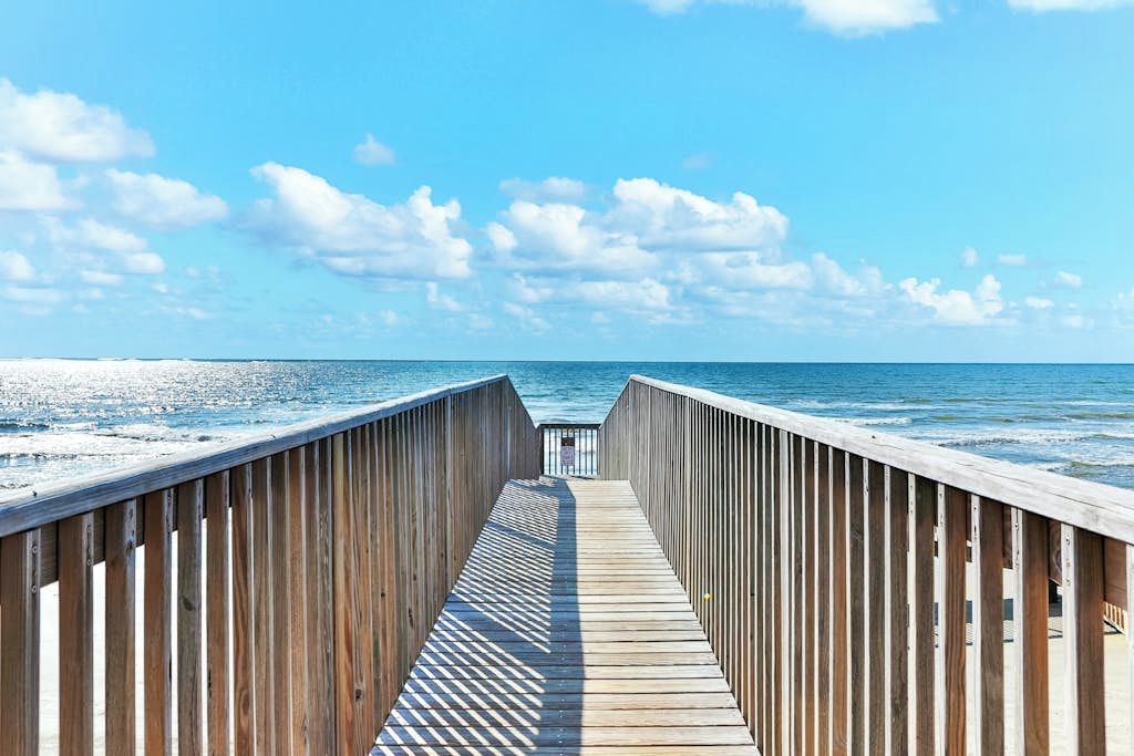A wooden boardwalk leading to the ocean with a clear sky above.