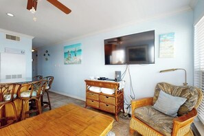 A living room with a flat-screen TV, wicker furniture, and a dining area with chairs and a table. - Seascape Condos #1201 (Galveston)