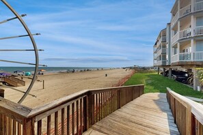 A beach view with a wooden deck, a large wheel structure, and a building with balconies. - Seascape Condos #1201 (Galveston)