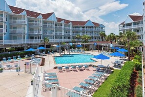 A hotel with a swimming pool, sun loungers, and a covered area with umbrellas. - Seascape Condos #1201 (Galveston)