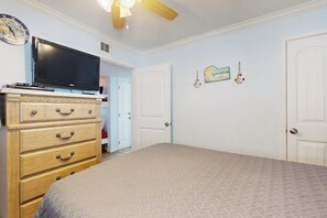 A bedroom with a bed, dresser, television, and a door leading to another room. - Seascape Condos #1201 (Galveston)