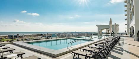 A rooftop pool with sunbathing areas and a view of the ocean.