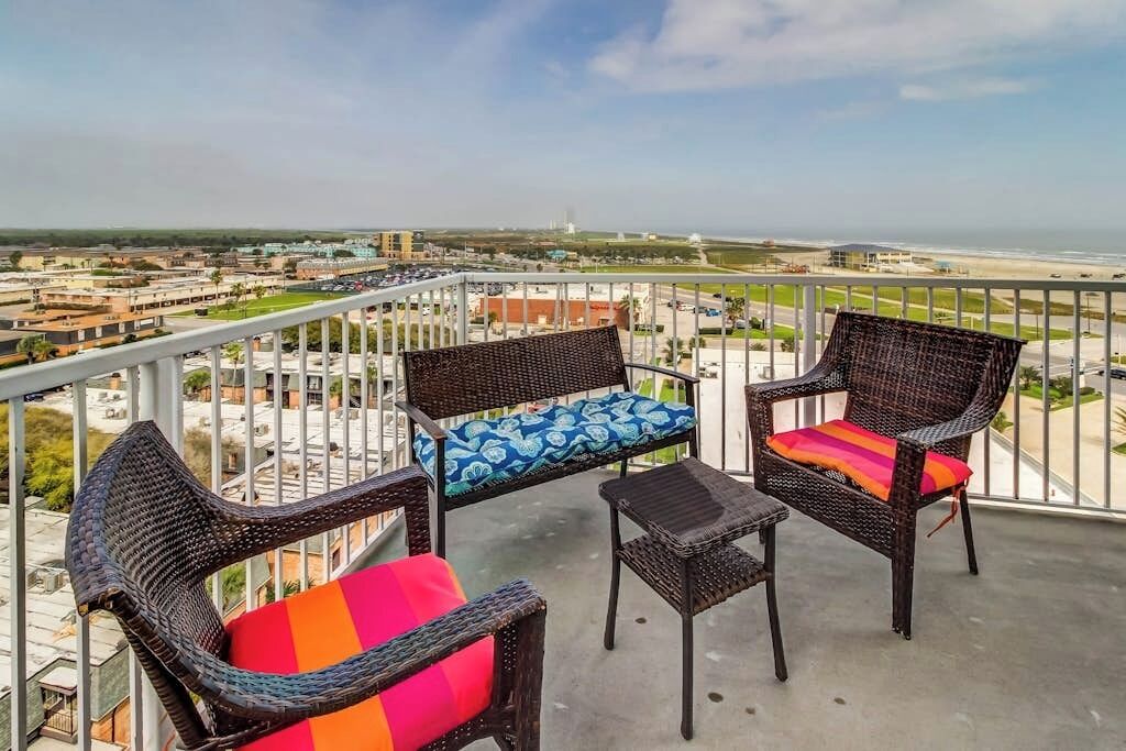 A balcony with wicker furniture and a view of a coastal area.