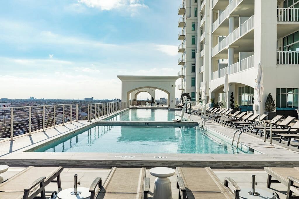 A rooftop pool with a view of the city, lounge chairs, and a white building with balconies.