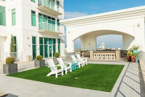 A rooftop patio with outdoor seating, a view of the city, and a building with balconies. - Emerald by the Sea #806 (Galveston)