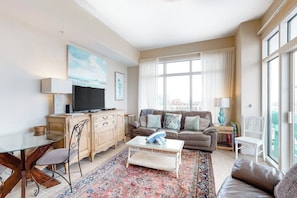 A living room with a sofa, a coffee table, a television, and a large window. - Emerald by the Sea #806 (Galveston)