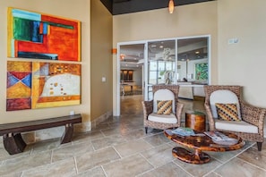 A lobby with a bench, two wicker chairs with cushions, a coffee table, and abstract art on the wall. - Emerald by the Sea #806 (Galveston)