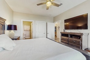 A bedroom with a large bed, a ceiling fan, a flat-screen TV, and a dresser. - Pointe West Resort - Treasure on the Beach (Galveston)