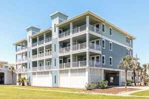 A multi-story residential building with balconies, a garage, and a well-maintained lawn. - Pointe West Resort - Treasure on the Beach (Galveston)