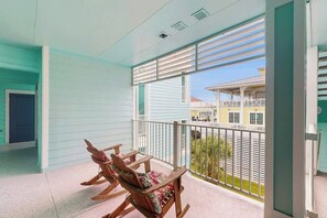 A balcony with a view of a building and a fence. There are two rocking chairs and a table. - Pointe West Resort - Treasure on the Beach (Galveston)
