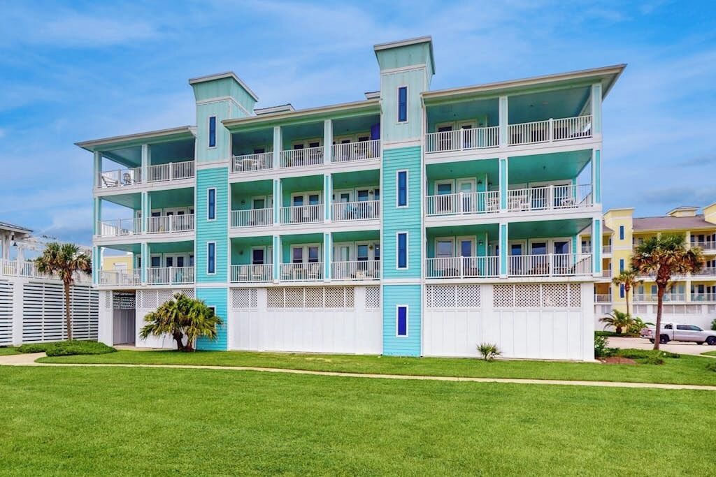 Ein mehrstöckiges Hotel mit Balkonen, einem weißen Zaun und einem gepflegten Rasen.
