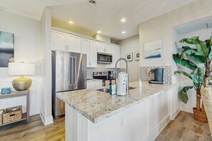 A modern kitchen with white cabinetry, stainless steel appliances, a granite countertop, and a large island. - Pointe West Resort - Treasure on the Beach (Galveston)