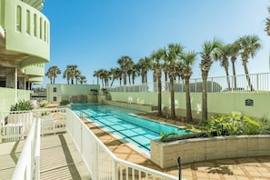 A swimming pool with a tiled deck, surrounded by palm trees and a white fence. - Seaside Oasis - Gulf Views, Pool & Fishing Pier (Galveston)