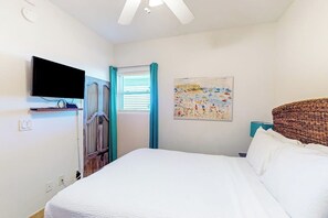 A bedroom with a bed, a television mounted on the wall, a painting, and a window with curtains. - Seaside Oasis - Gulf Views, Pool & Fishing Pier (Galveston)