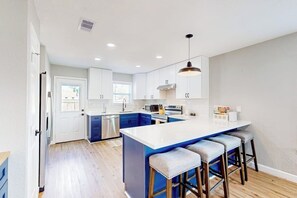 A modern kitchen with a central island, bar stools, and a view to the outside. - Out of the Blue - Fire Pit & Patio Near the Beach (Galveston)