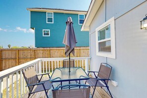 A deck with a table and chairs, a covered umbrella, and a wooden fence. - Out of the Blue - Fire Pit & Patio Near the Beach (Galveston)
