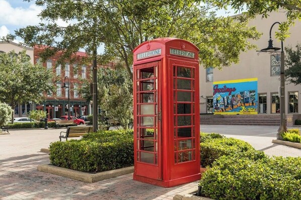 A red telephone booth in a public square with a mural in the background. - Diamond Beach Resort - Lazy River View #419 (Galveston)