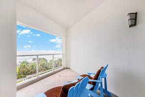 Een balkon met uitzicht op de oceaan, een blauwe stoel en een bruine stoel.