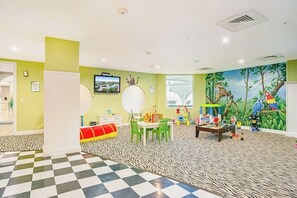 A children's playroom with a zebra-patterned floor, a television, and a mural of jungle animals. - Diamond Beach Resort - Lazy River View #419 (Galveston)