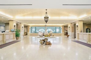 Eine geräumige Lobby mit einem zentralen Kronleuchter, einem Empfangsbereich und einer dekorativen Insellandschaft mit Muscheln und einem Seestern.