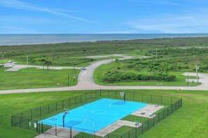 Un campo da basket all'aperto con recinzione, una strada e vista sull'oceano.