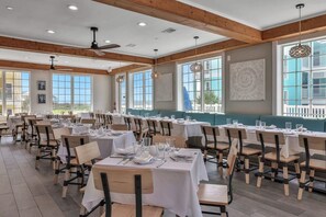A dining area with multiple tables and chairs, large windows, and ceiling fans. - Mannanan Mac Lir - Ocean View, Pool & Hot Tub (Galveston)