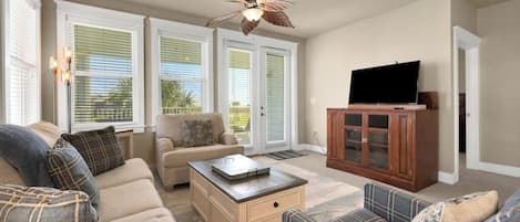 A living room with a sofa set, a coffee table, a television on a stand, and a ceiling fan.