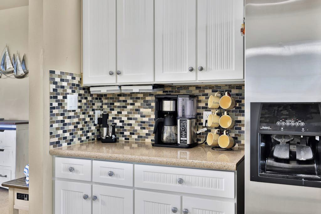 Una cocina con armarios blancos, cafetera, máquina de café y dispensador de agua.