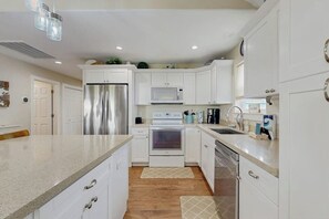A modern kitchen with white cabinets, stainless steel appliances, and a granite countertop. - Blue Sunrise - Bay Views, Pool & Dog-Friendly (Galveston)