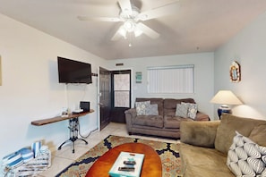 A living room with a ceiling fan, a flat-screen TV, two sofas, a coffee table, and a patterned rug. - Seahorse Condominiums 105 (Corpus Christi)