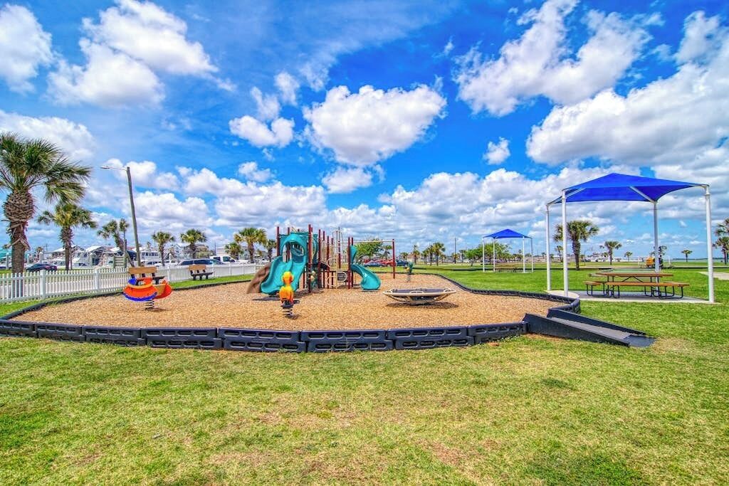 Un parque infantil con toboganes y estructuras para escalar, rodeado de césped y palmeras.