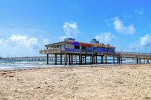 A pier extending into the ocean with a building on it, featuring a sign that reads 'Motel May's.' - Palm Bay 202 - Heated Pool, BBQ & Beach Access (Corpus Christi)