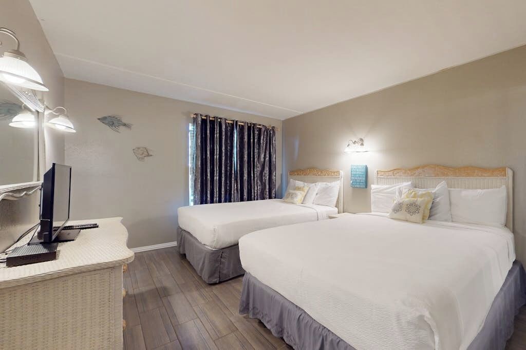 A hotel room with two beds, a desk with a computer, and a window with curtains.