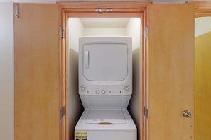 A compact, built-in washer and dryer unit with a control panel, enclosed in a wooden cabinet. - Sunchase Beachfront #130 (South Padre Island)