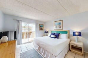A hotel room with a bed, two bedside tables, a TV, and a view of the outdoors. - Fiesta Sol Condominiums #109 (South Padre Island)