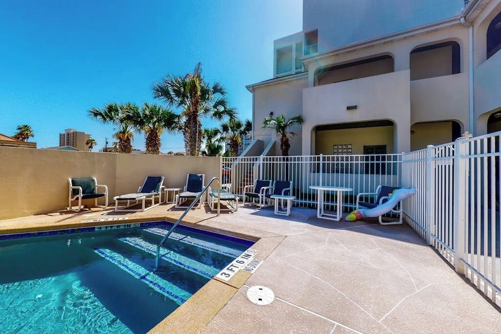 A swimming pool with lounge chairs and a sunbed, surrounded by a white fence.