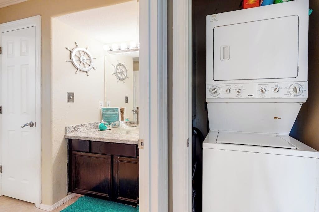 A laundry room with a washing machine and dryer, a sink with a mirror, and a door leading to another room.