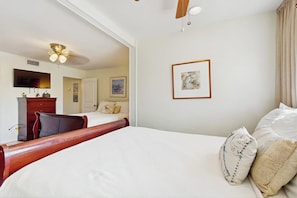Ett hotellrum med en säng, en byrå, en takfläkt och en inramad tavla på väggen.
