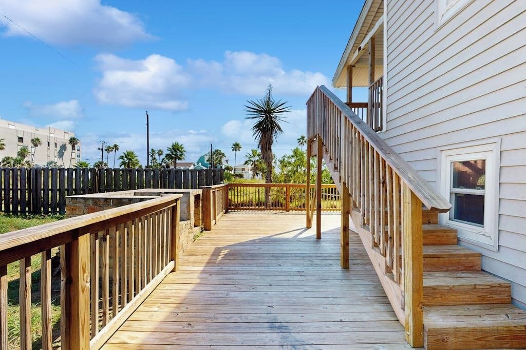 A wooden deck leading to a white house with a staircase.