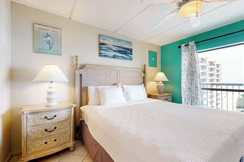A bedroom with a large bed, two bedside tables with lamps, a headboard, and artwork on the walls.