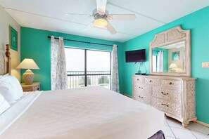 A bedroom with a large bed, a ceiling fan, a dresser, a TV, and a window with curtains. - Saida Towers III #3116 (South Padre Island)