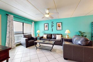 Ein Wohnzimmer mit zwei Sofas, einem Couchtisch, einem Deckenventilator und einem Fenster mit Vorhängen.